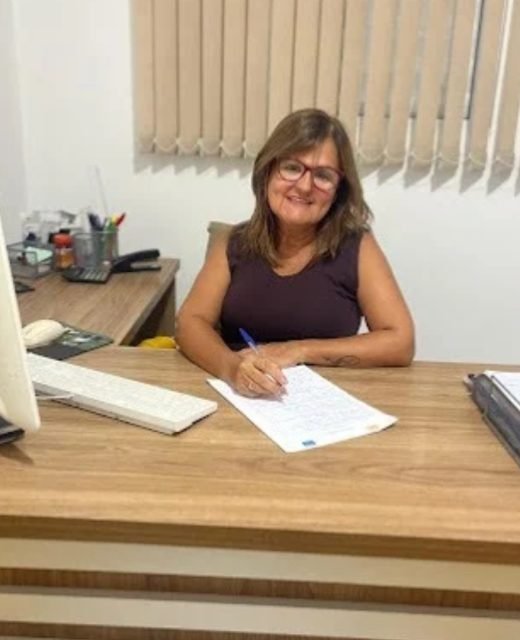 Dra. Silvana Lima, advogada trabalhista em Praia Grande, sorrindo em seu escritório enquanto assina documentos em sua mesa de trabalho. Título