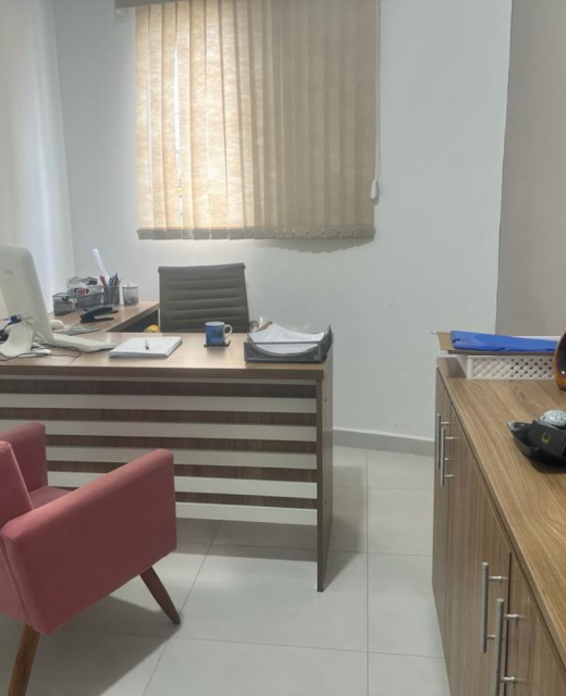 Interior de escritório de advocacia moderno com mesa de madeira, computador, poltrona rosa para clientes e decoração clean.